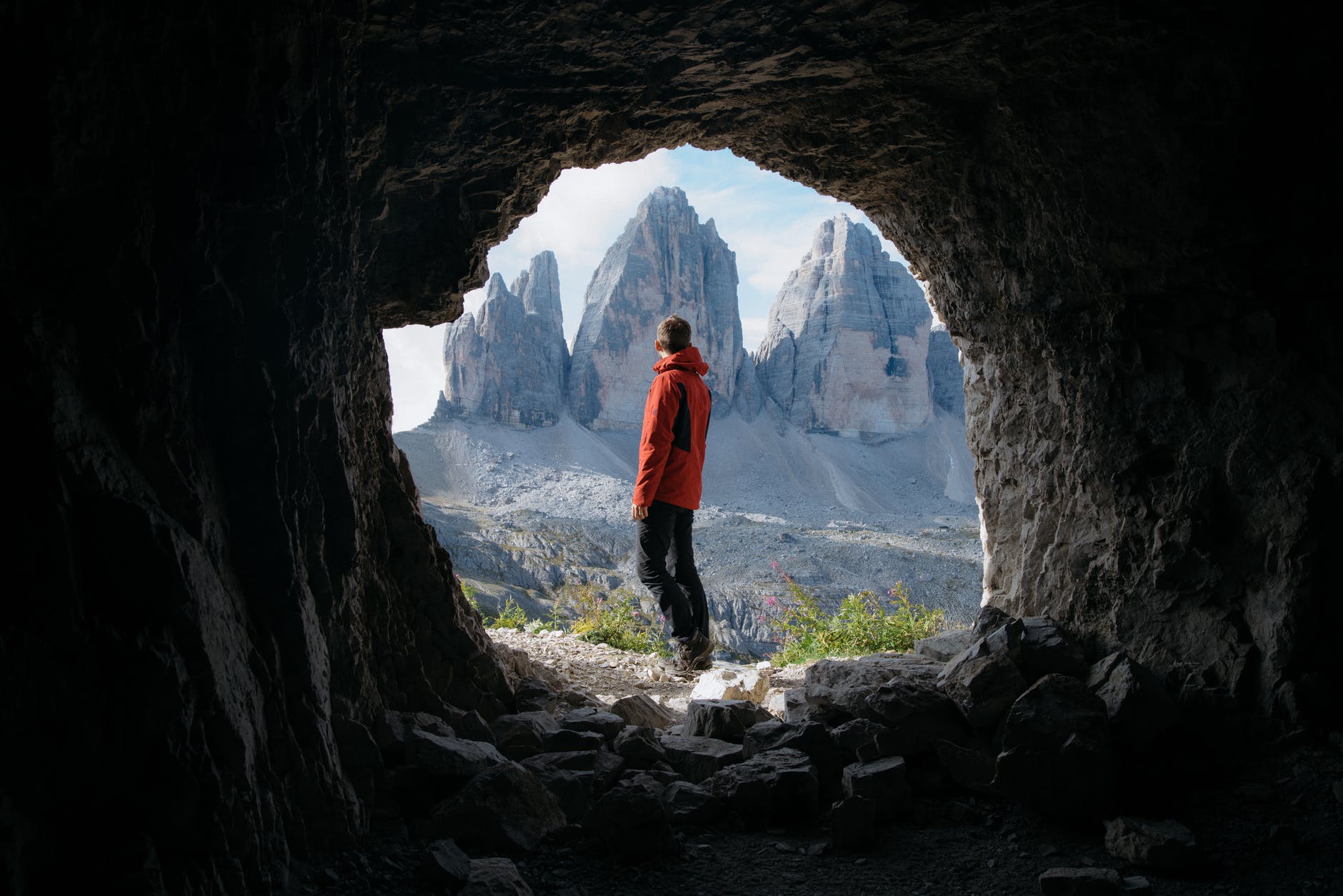 man in red jacket standing outside of the cave across the three mountains